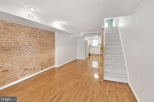 below grade area with brick wall, freestanding refrigerator, wood finished floors, stairs, and baseboards