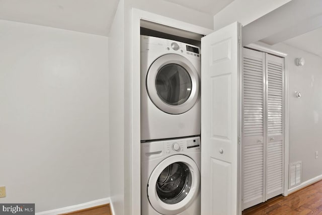 laundry area with stacked washer / dryer, wood finished floors, and baseboards