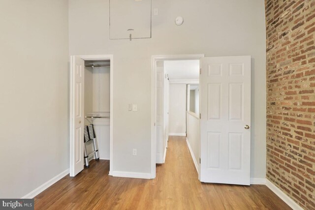 unfurnished bedroom with wood finished floors, baseboards, and brick wall
