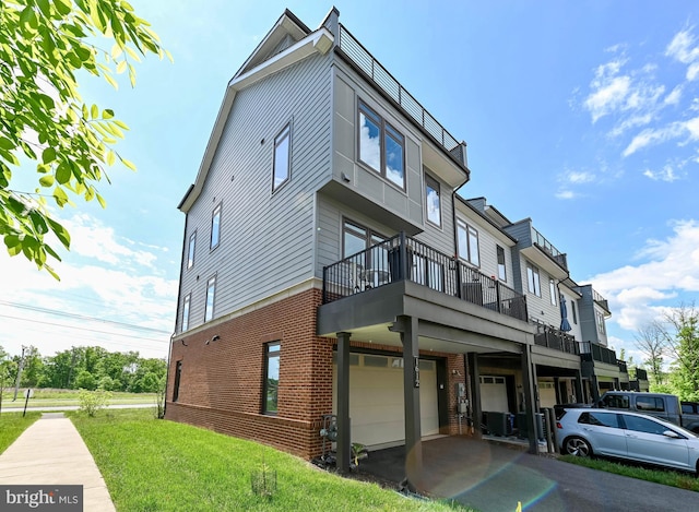 view of front of home featuring a garage, brick siding, a balcony, a front lawn, and driveway