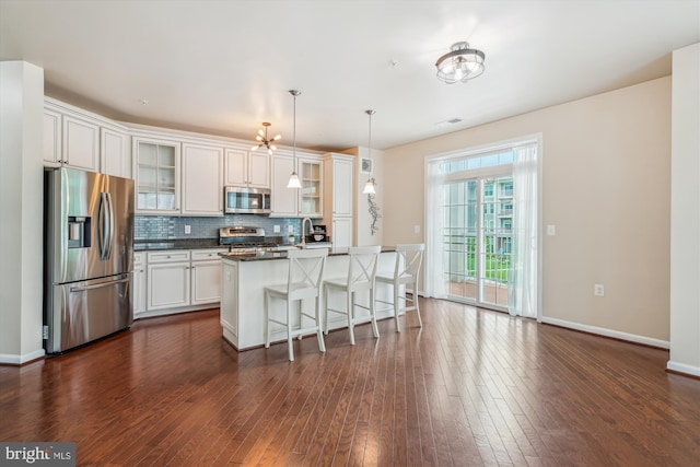 kitchen with stainless steel appliances, dark countertops, decorative backsplash, a breakfast bar, and dark wood finished floors
