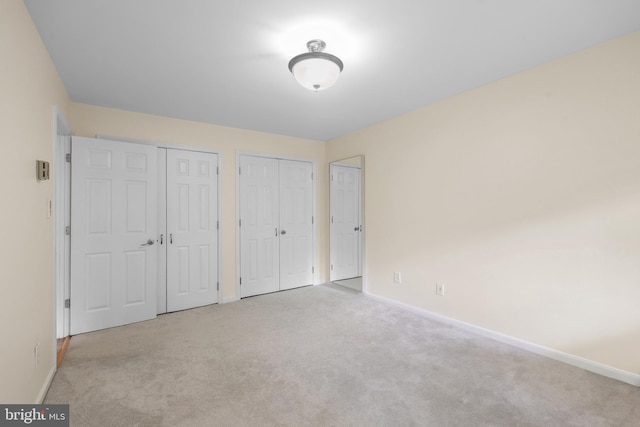 unfurnished bedroom with multiple closets, carpet floors, and baseboards