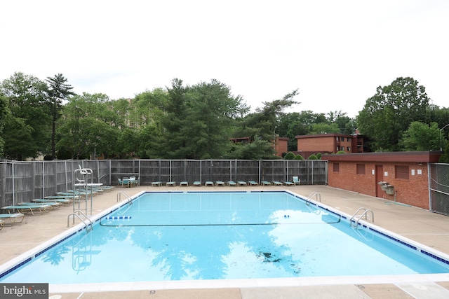 community pool with fence, a patio, and view of scattered trees