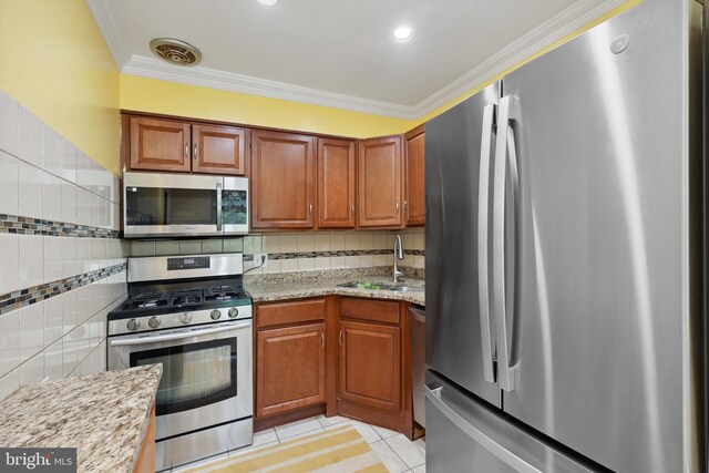 kitchen with appliances with stainless steel finishes, a sink, light tile patterned flooring, ornamental molding, and brown cabinets