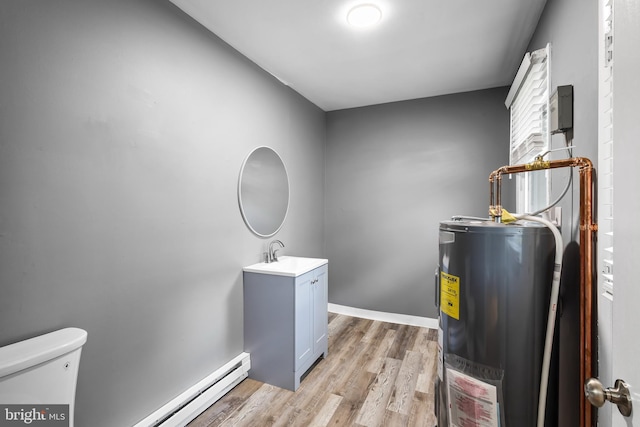clothes washing area with electric water heater, a sink, light wood finished floors, a baseboard heating unit, and baseboards