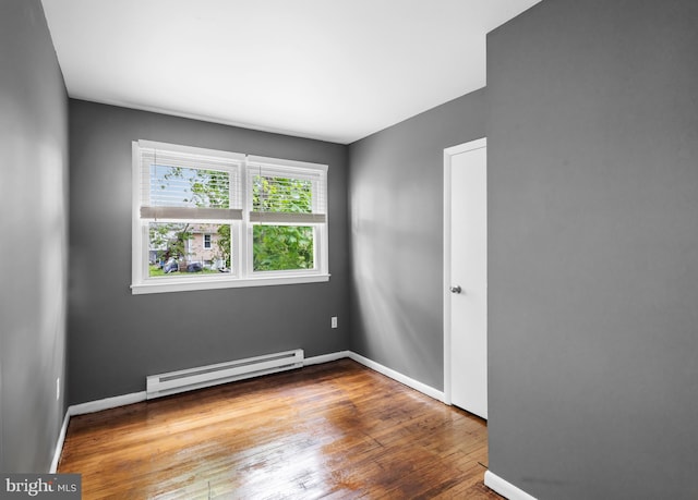 spare room featuring baseboard heating, wood finished floors, and baseboards