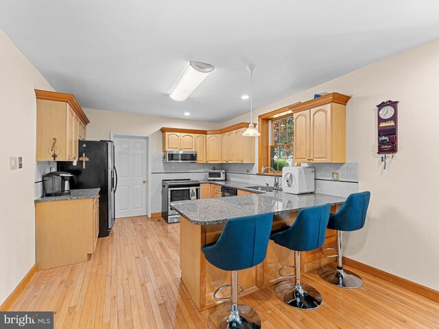 kitchen featuring appliances with stainless steel finishes, a sink, a peninsula, light brown cabinetry, and a breakfast bar