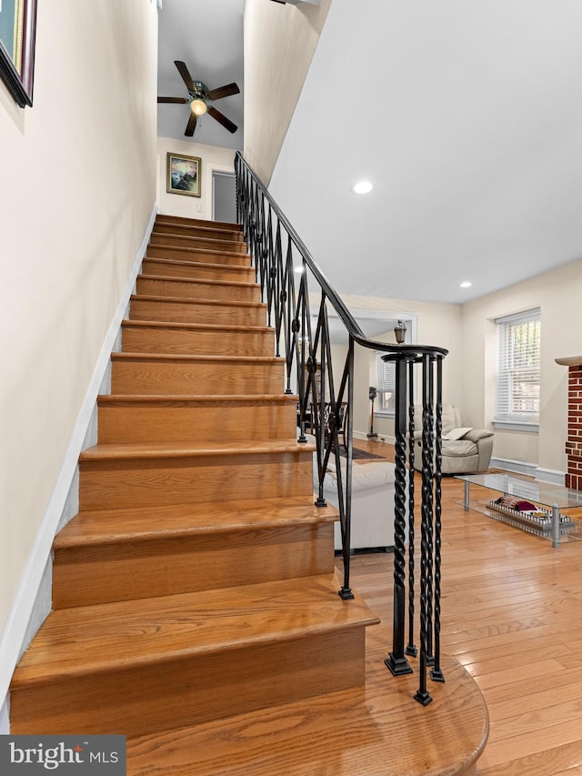 stairs featuring a ceiling fan, wood finished floors, recessed lighting, baseboards, and a brick fireplace