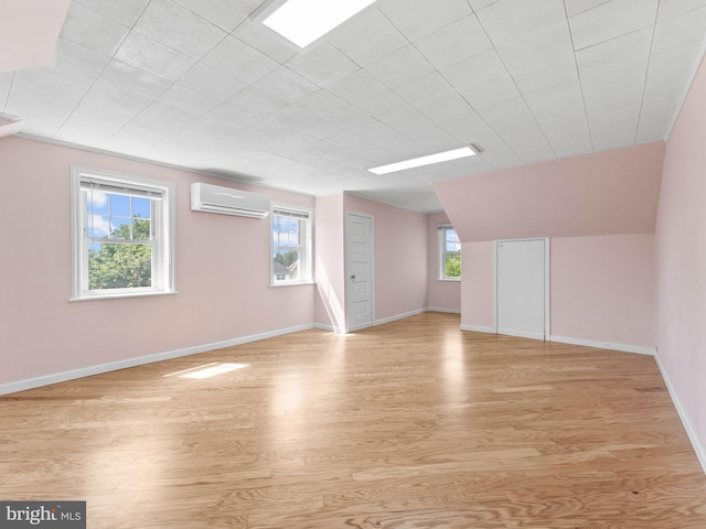 bonus room featuring a wall mounted AC, light wood-style flooring, baseboards, and lofted ceiling