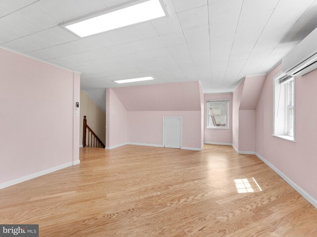 additional living space featuring light wood-style floors, a wall mounted AC, baseboards, and vaulted ceiling