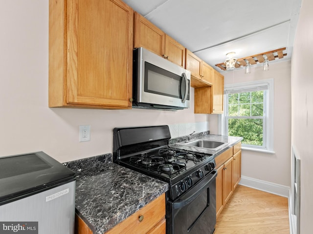 kitchen featuring stainless steel microwave, gas stove, a sink, light wood-style flooring, and baseboards