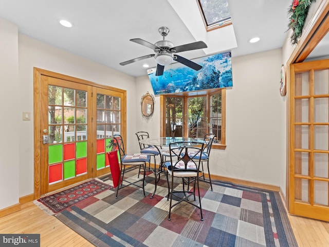dining space featuring a skylight, ceiling fan, baseboards, wood finished floors, and recessed lighting