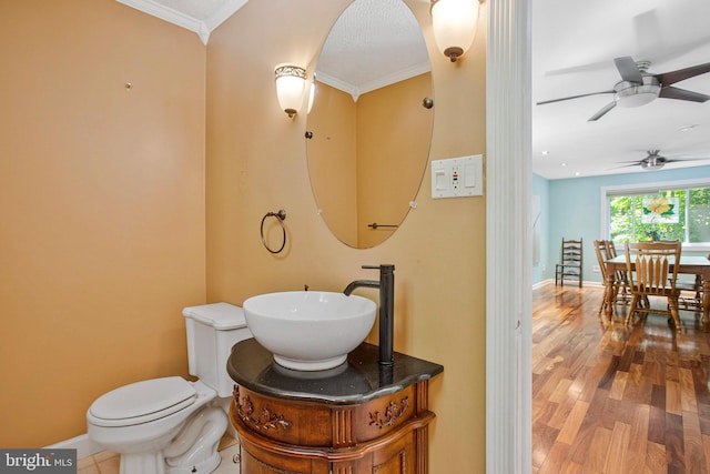 half bathroom with ornamental molding, toilet, wood finished floors, baseboards, and ceiling fan