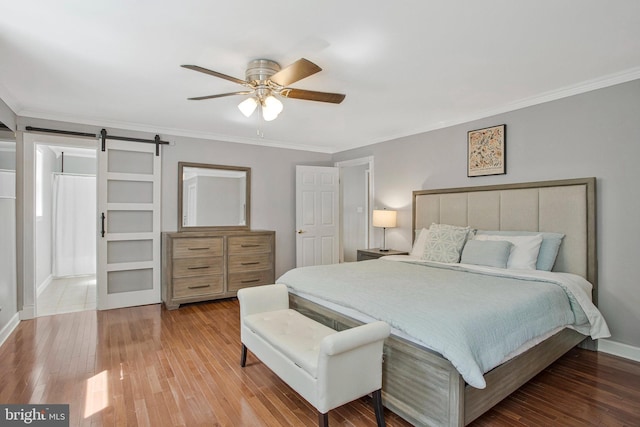bedroom with a barn door, hardwood / wood-style floors, crown molding, baseboards, and a ceiling fan
