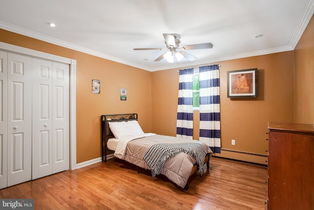 bedroom with baseboard heating, wood finished floors, baseboards, crown molding, and a closet