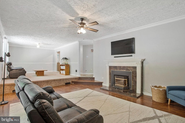 living area with wood finished floors, crown molding, ceiling fan, a premium fireplace, and baseboards
