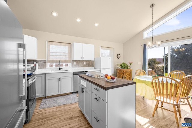 kitchen featuring butcher block countertops, an inviting chandelier, a sink, decorative backsplash, and stainless steel appliances