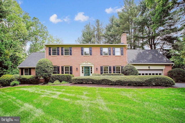 colonial house featuring a chimney, an attached garage, brick siding, and a front yard