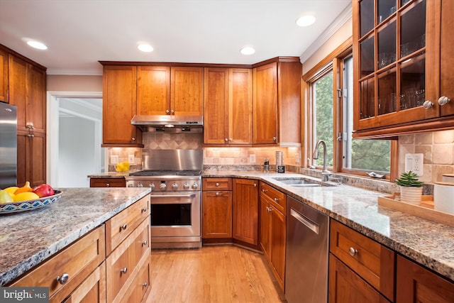 kitchen featuring appliances with stainless steel finishes, a sink, under cabinet range hood, ornamental molding, and light wood-type flooring