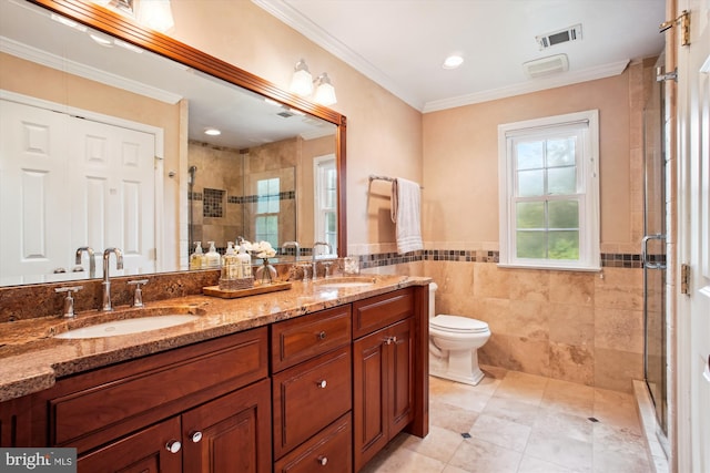 full bath with tile walls, a shower stall, double vanity, crown molding, and tile patterned floors