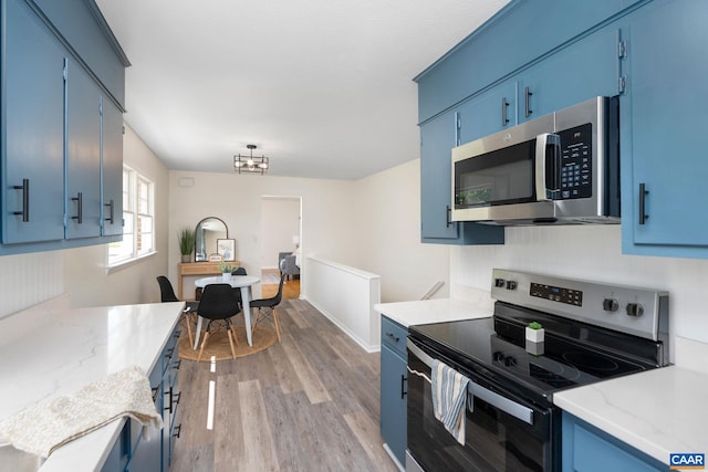 kitchen featuring blue cabinets, appliances with stainless steel finishes, a chandelier, light stone countertops, and light wood-style floors