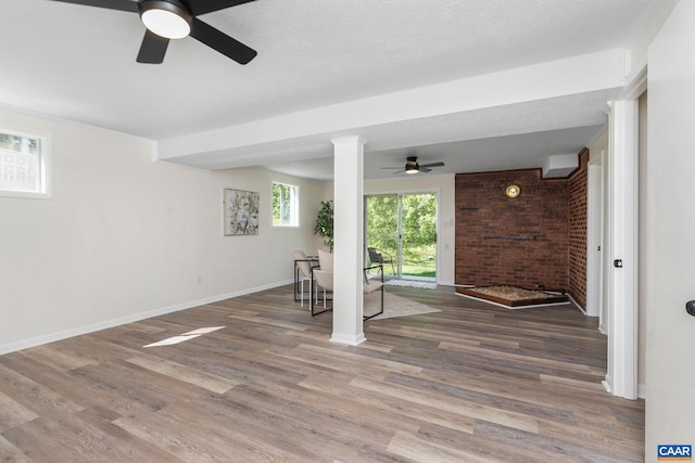 unfurnished living room with baseboards, brick wall, ceiling fan, and wood finished floors