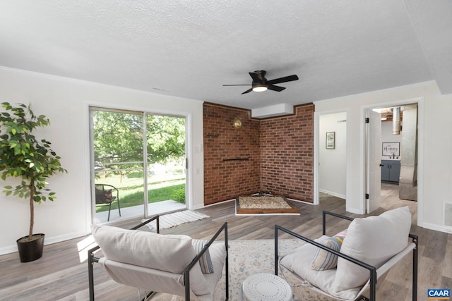 living room with wood finished floors, brick wall, a textured ceiling, baseboards, and ceiling fan