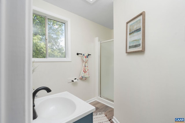 bathroom with baseboards, wood finished floors, a shower stall, and a sink