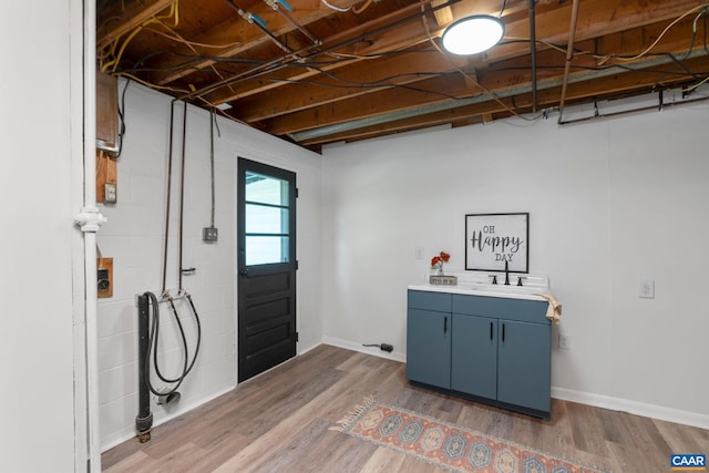 laundry room with a sink, cabinet space, baseboards, and wood finished floors