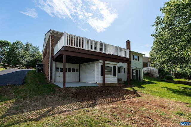 back of property with a yard, dirt driveway, an attached garage, and a chimney