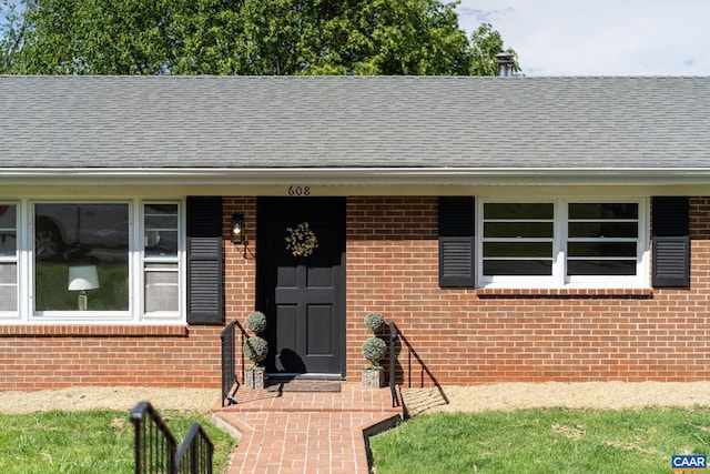 doorway to property with roof with shingles and brick siding