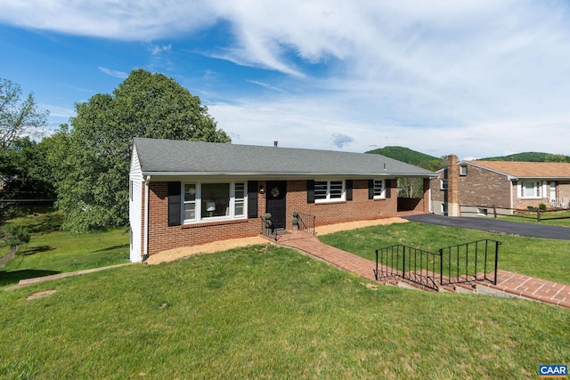 ranch-style home with driveway, a shingled roof, brick siding, and a front yard
