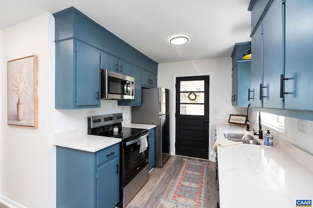 kitchen featuring a sink, blue cabinets, stainless steel appliances, and light wood-style floors