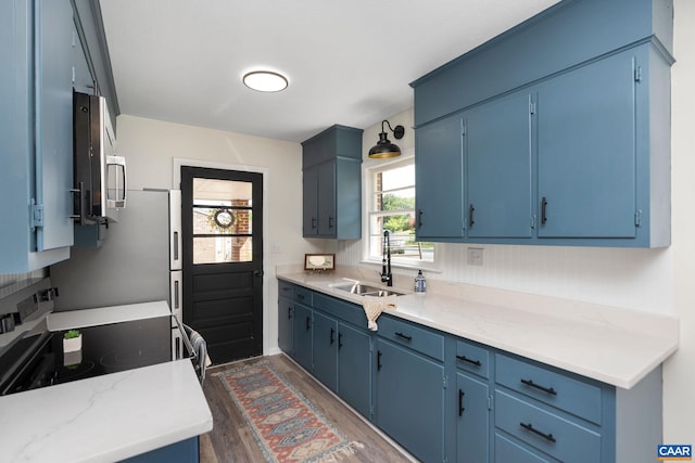 kitchen featuring a sink, stainless steel appliances, blue cabinetry, and dark wood finished floors