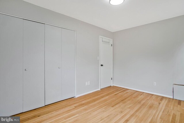 unfurnished bedroom featuring wood finished floors, baseboards, and a closet