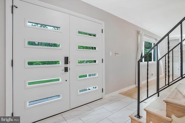 entrance foyer featuring stairs, light marble finish flooring, and baseboards