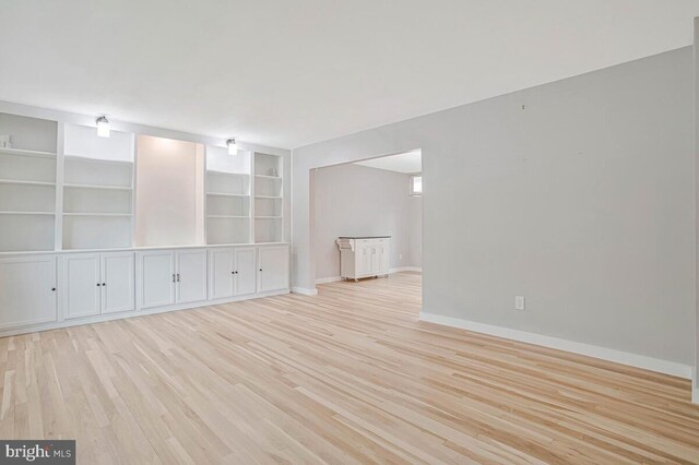 empty room with light wood-style floors, baseboards, and built in shelves
