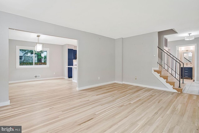 unfurnished living room with light wood finished floors, baseboards, and stairway