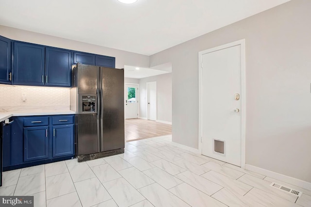 kitchen featuring black refrigerator with ice dispenser, blue cabinets, light countertops, backsplash, and baseboards