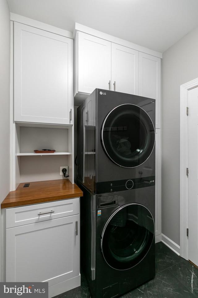 10609 Little Run Farm Ct, Vienna, VA 22182 - laundry room featuring stacked washer and clothes dryer, cabinet space, dark marble finish flooring, and baseboards