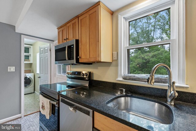 kitchen featuring dark stone countertops, a sink, stainless steel appliances, baseboards, and washer / dryer