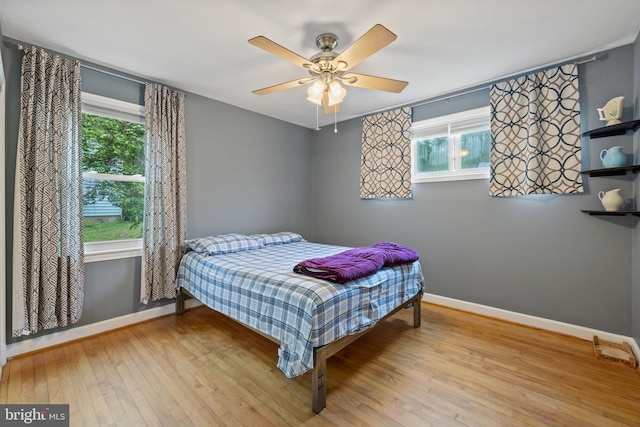 bedroom featuring multiple windows, baseboards, ceiling fan, and hardwood / wood-style flooring