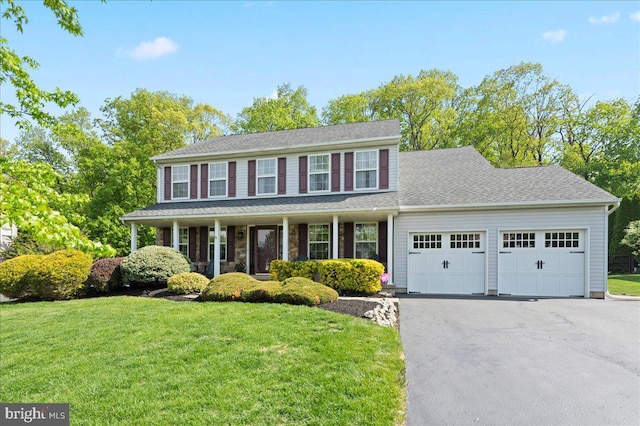 colonial-style house featuring a garage, a front lawn, asphalt driveway, and a porch