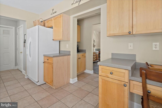 kitchen with light tile patterned floors, light brown cabinetry, white refrigerator with ice dispenser, and baseboards