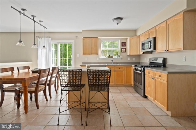 kitchen featuring appliances with stainless steel finishes, light brown cabinetry, light tile patterned floors, a breakfast bar, and a center island