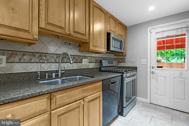 kitchen with stainless steel appliances, a sink, dark stone countertops, backsplash, and light tile patterned flooring