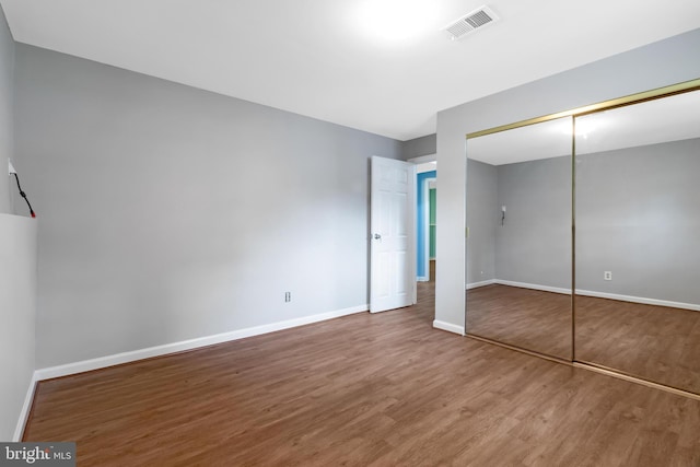 unfurnished bedroom featuring wood finished floors, baseboards, and a closet