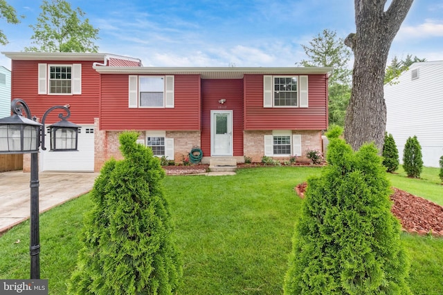 raised ranch featuring driveway, a front yard, and brick siding