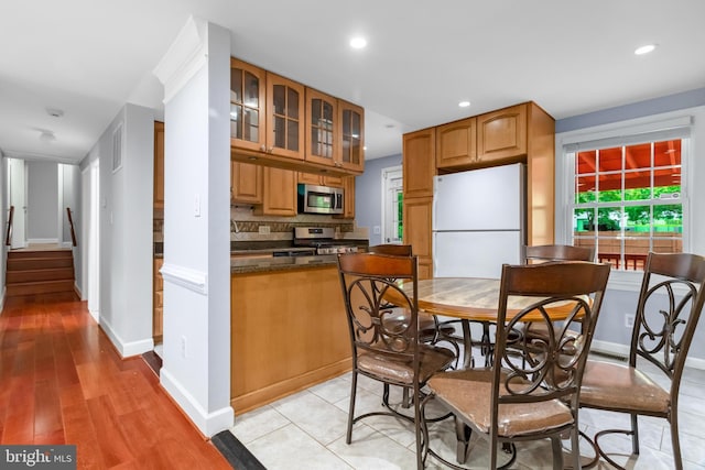 kitchen with appliances with stainless steel finishes, glass insert cabinets, dark countertops, decorative backsplash, and recessed lighting