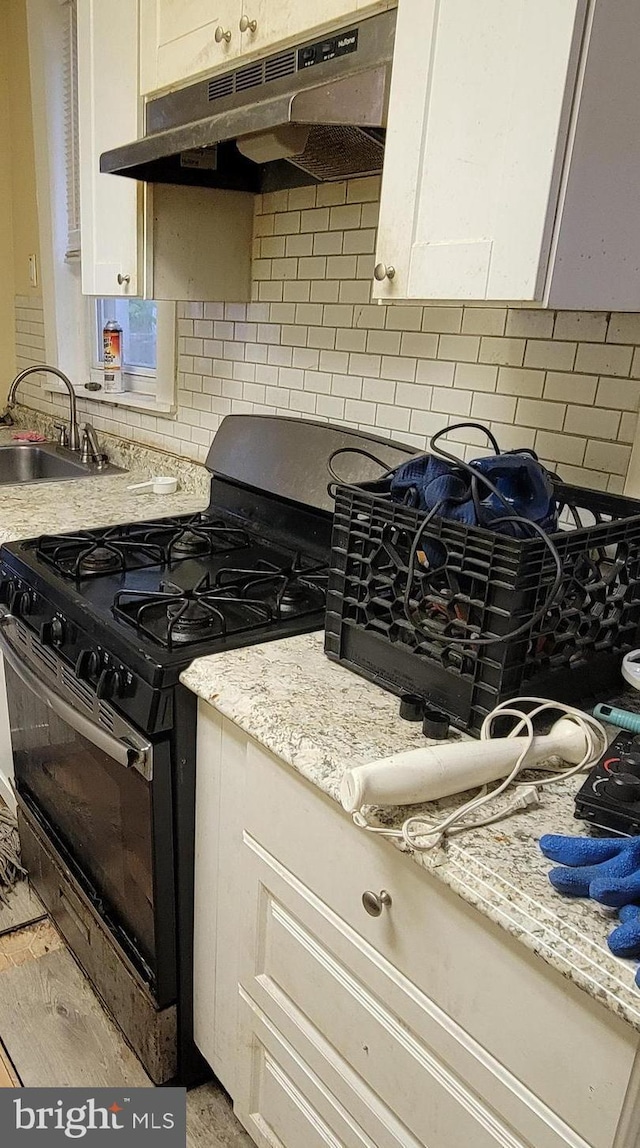 kitchen featuring gas stove, under cabinet range hood, decorative backsplash, a sink, and light stone countertops